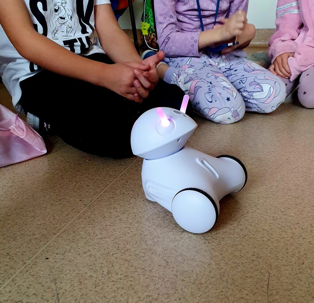 Robocik. Z tyłu dzieci siedzące na podłodze.